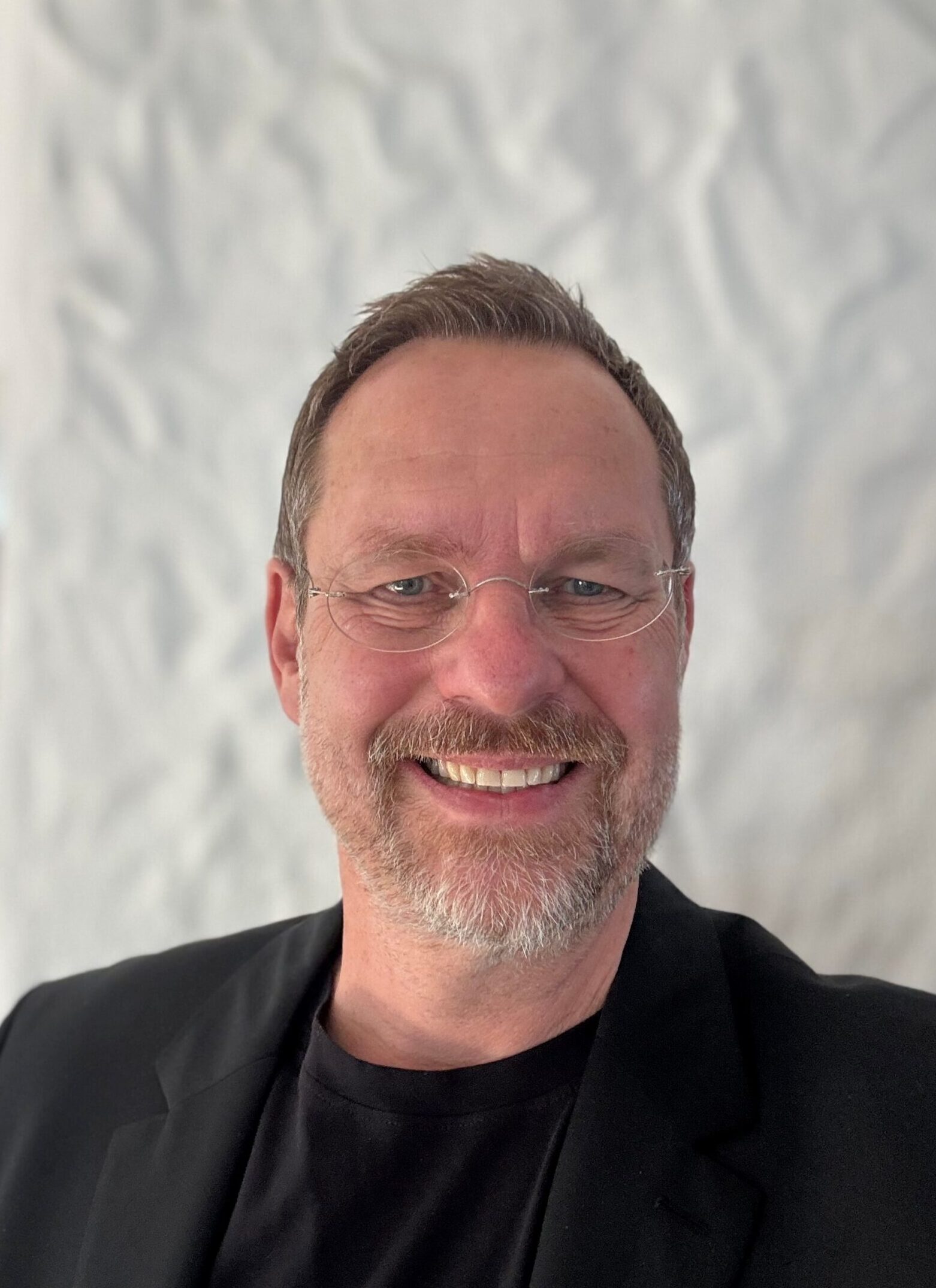 Lächelnder Mann mit Brille vor weißer Wand.