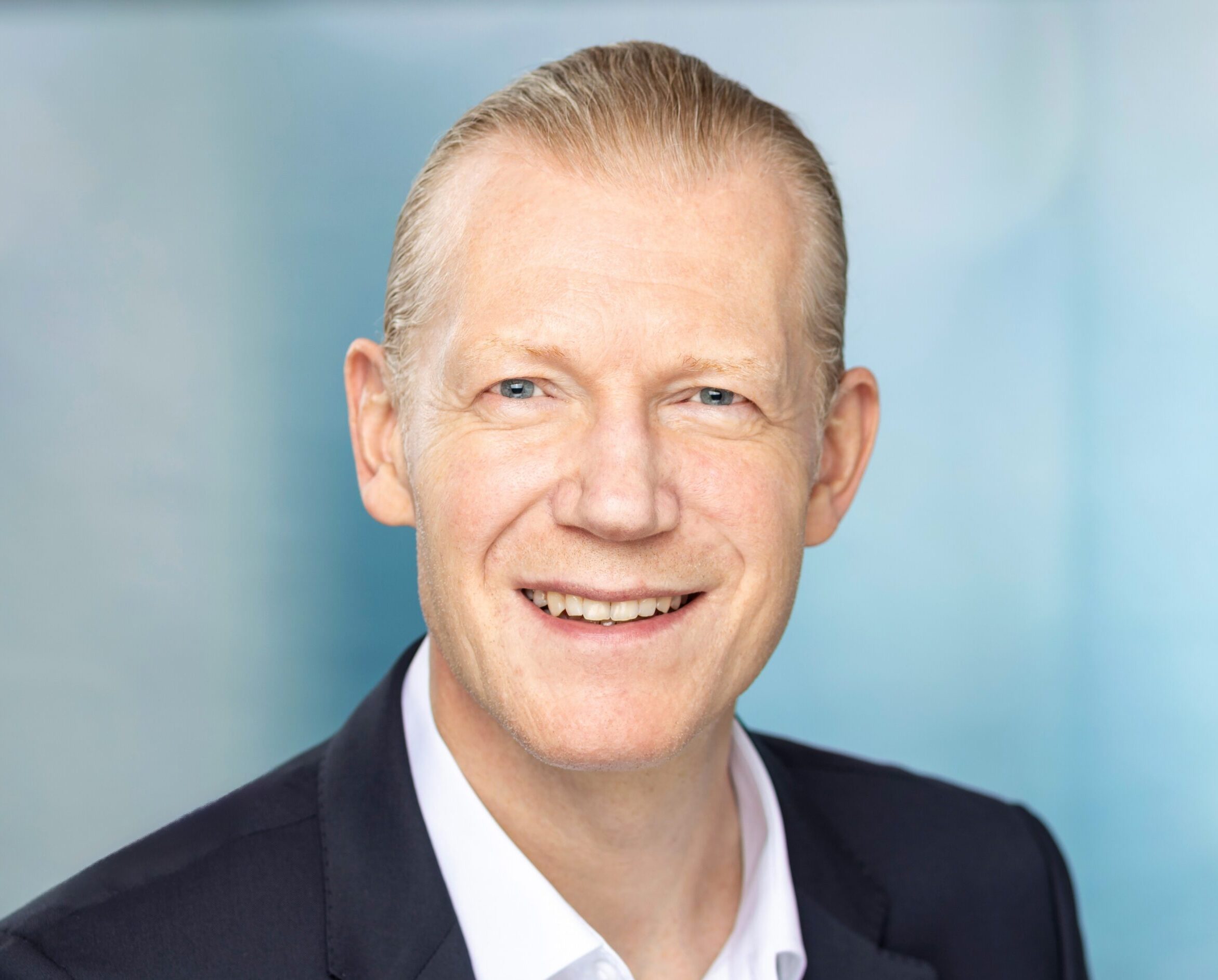 Mann im Anzug lächelt vor blauem Hintergrund.