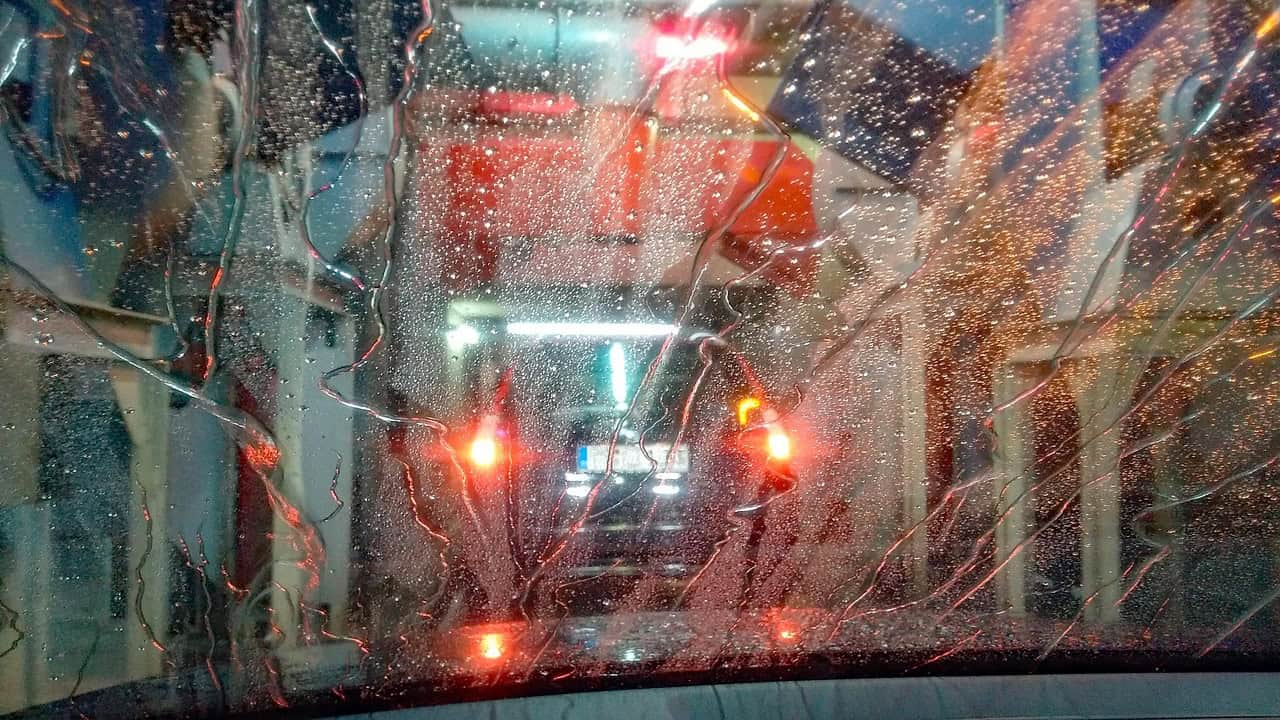 Auto durchfährt Waschanlage, Wasser tropft auf Scheibe.