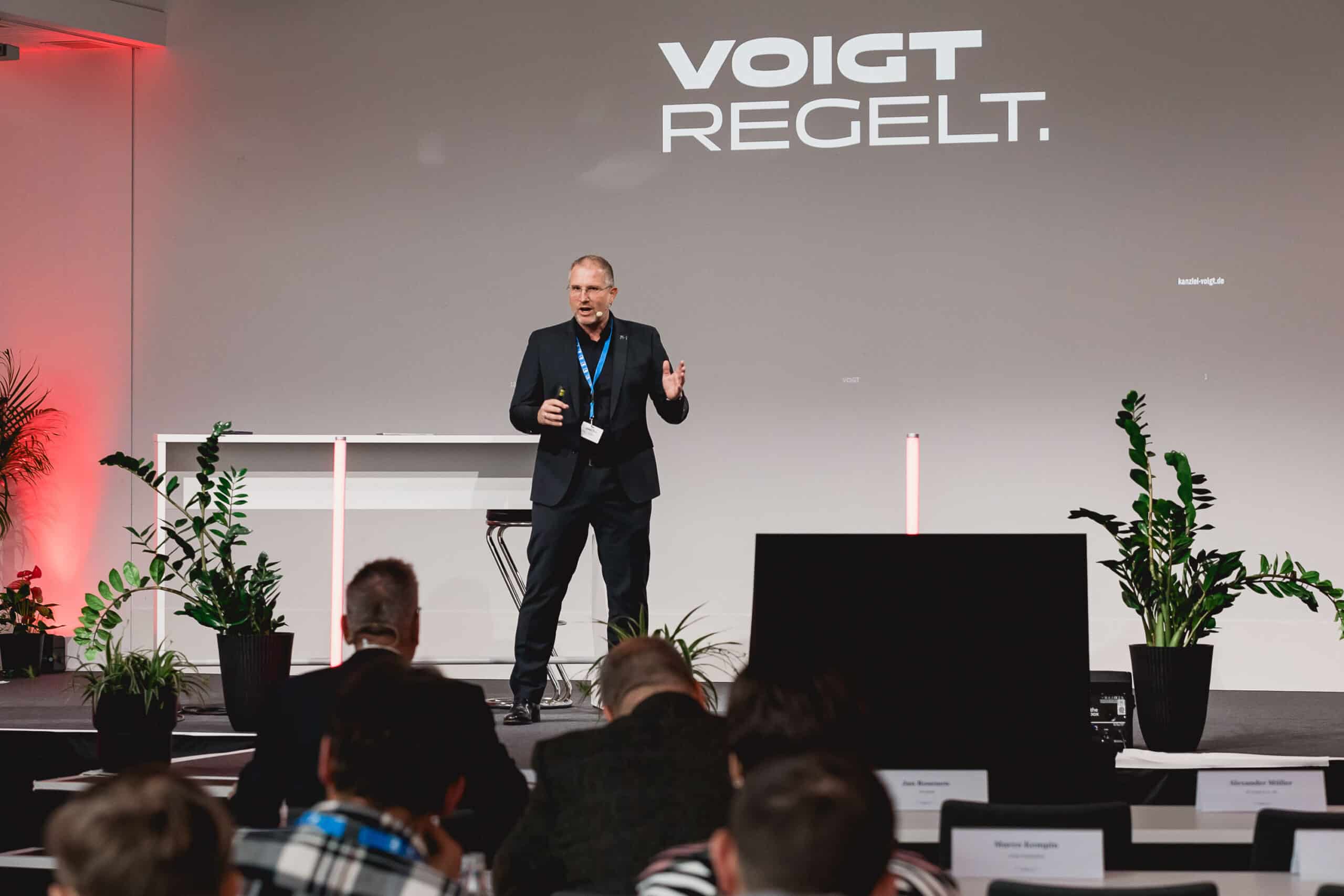 Redner auf einer Konferenzbühne mit Publikum.