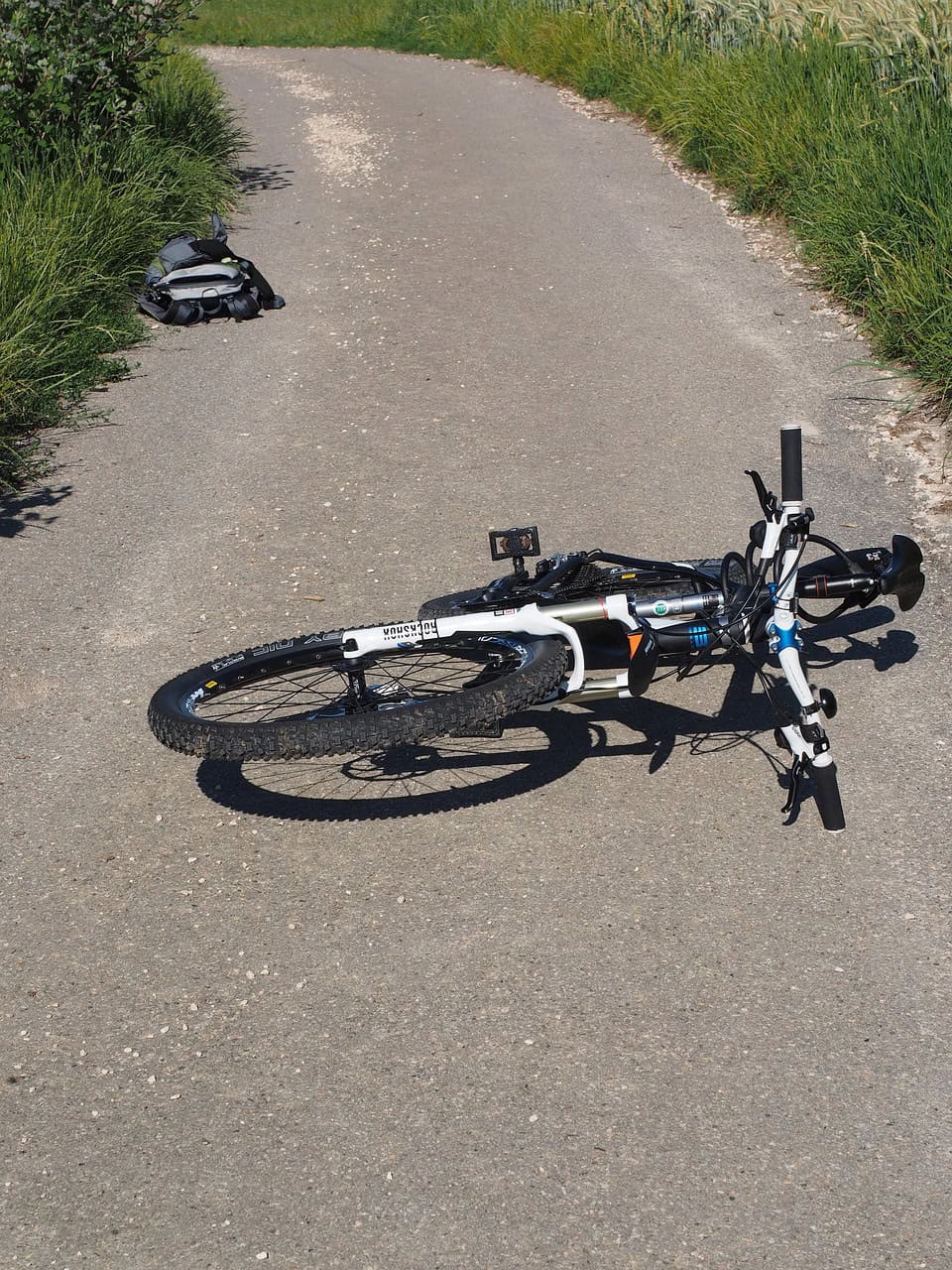 Wegeunfall? Fahrrad liegt auf asphaltierter Landstraße neben Rucksack.
