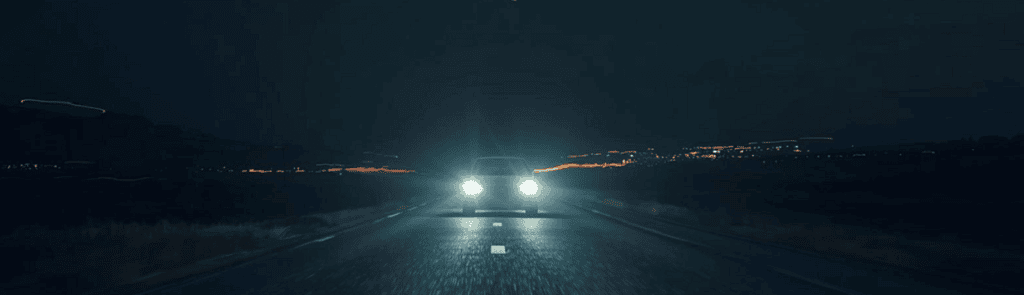 Auto fährt nachts mit aufgeblendeten Scheinwerfern auf Landstraße.