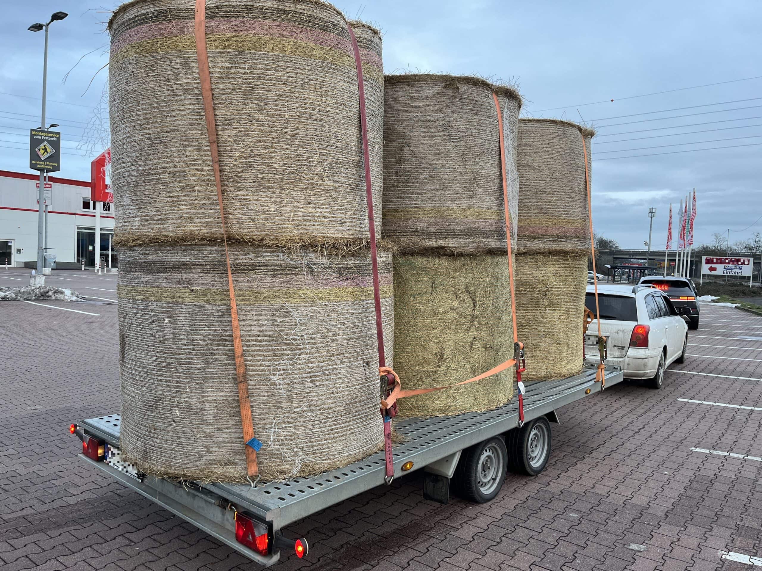Auto mit Anhänger voller Heuballen im Parkplatz.